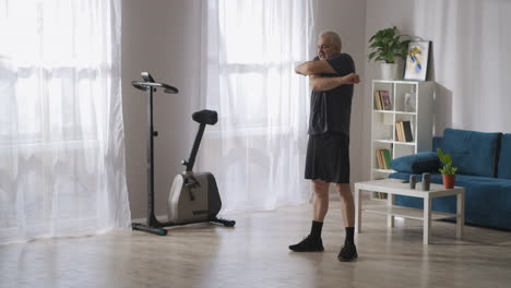 middle-aged-adult-man-is-training-alone-in-his-apartment-at-morning-waving-hands-warming-muscles